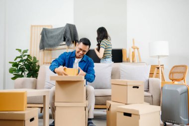 Büyük kutuları olan genç bir çift yeni bir eve taşınıyor, çift için yeni bir daire, genç Asyalı erkek ve kadın yeni ev için kanepenin taşınmasına yardım ediyorlar.