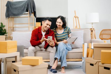 Asyalı genç ve çekici bir çift, yeni evlerinde tablet ve akıllı telefon, alışveriş mobilyaları, karton paketlerle dekore edilmiş evler kullanıyor. Genç evli Asyalı eve taşınıyor..