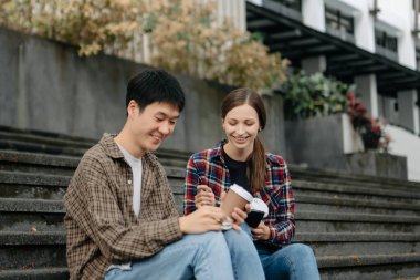 Üç genç üniversite öğrencisi, kampüs parkında arkadaşlarıyla çimde otururken rahatlarken kitap okuyor. Sabah eğitim kavramı