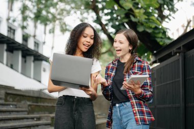 Üç genç üniversite öğrencisi, kampüs parkında arkadaşlarıyla çimde otururken rahatlarken kitap okuyor. Sabah eğitim kavramı