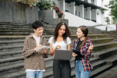 Üç genç üniversite öğrencisi, kampüs parkında arkadaşlarıyla çimde otururken rahatlarken kitap okuyor. Sabah eğitim kavramı