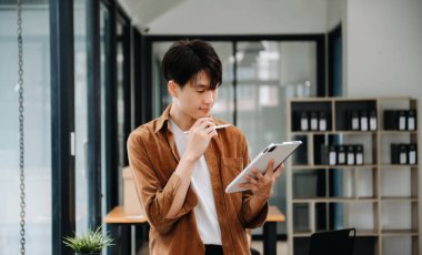 Modern ofiste laptopla, tabletle çalışan ve kağıda not alan genç bir iş adamı..