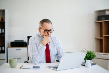 Laptop, tablet ve notlarla modern ofiste çalışan kıdemli işadamı. İş, finans, düşünme, liderlik ve işyeri teknolojisi kavramı.