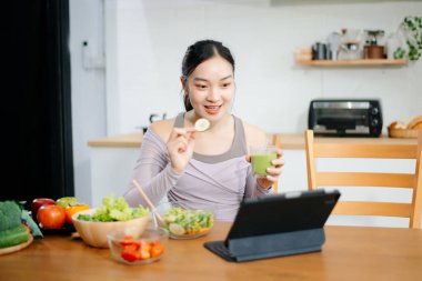 Modern bir mutfakta, taze meyve, sebze, blender ve meyve suyuyla gülümseyen bir kadın. Temiz yemek, sağlıklı yaşam ve hayat dolu bir yaşam tarzı..
