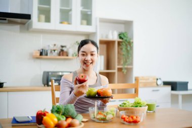 Modern bir mutfakta, taze meyve, sebze, blender ve meyve suyuyla gülümseyen bir kadın. Temiz yemek, sağlıklı yaşam ve hayat dolu bir yaşam tarzı..