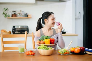 Modern bir mutfakta, taze meyve, sebze, blender ve meyve suyuyla gülümseyen bir kadın. Temiz yemek, sağlıklı yaşam ve hayat dolu bir yaşam tarzı..