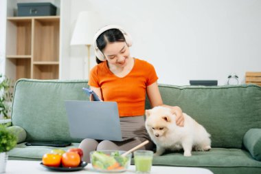 Beyaz kanepede oturan genç bir kadın oturma odasında küçük beyaz bir köpek yavrusu tutuyor.