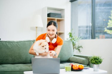 Beyaz kanepede oturan genç bir kadın oturma odasında küçük beyaz bir köpek yavrusu tutuyor.