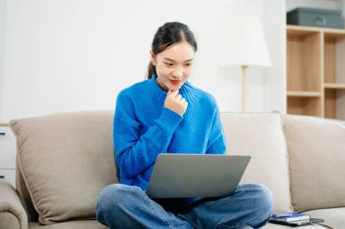 Genç Asyalı kadın akıllı telefon ve tablet kullanarak evdeki kanepede dinleniyor. Neşeli online alışveriş, dijital yaşam tarzı, ve rahat modern bir yaşam alanında kablosuz teknoloji..