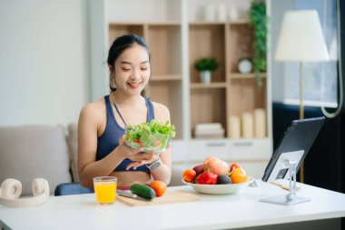 Neşeli bir kadın olarak sağlıklı beslenme, taze üretim ve sağlığın canlı bir sahnesi evde teknolojiyle uğraşırken salata ve meyvelerin tadını çıkarıyor.