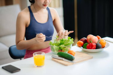 Neşeli bir kadın olarak sağlıklı beslenme, taze üretim ve sağlığın canlı bir sahnesi evde teknolojiyle uğraşırken salata ve meyvelerin tadını çıkarıyor.