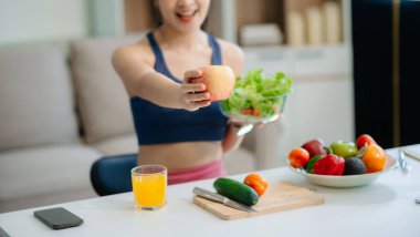 Neşeli bir kadın olarak sağlıklı beslenme, taze üretim ve sağlığın canlı bir sahnesi evde teknolojiyle uğraşırken salata ve meyvelerin tadını çıkarıyor.