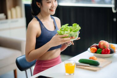 Neşeli bir kadın olarak sağlıklı beslenme, taze üretim ve sağlığın canlı bir sahnesi evde teknolojiyle uğraşırken salata ve meyvelerin tadını çıkarıyor.