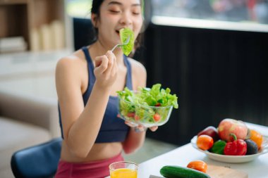 Neşeli bir kadın olarak sağlıklı beslenme, taze üretim ve sağlığın canlı bir sahnesi evde teknolojiyle uğraşırken salata ve meyvelerin tadını çıkarıyor.