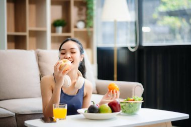 Neşeli bir kadın olarak sağlıklı beslenme, taze üretim ve sağlığın canlı bir sahnesi evde teknolojiyle uğraşırken salata ve meyvelerin tadını çıkarıyor.