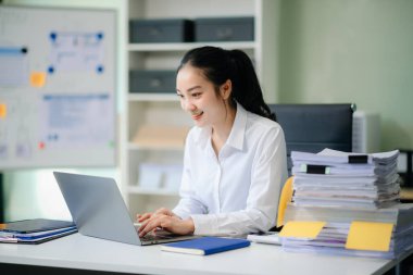 Çalışan not defteri, tablet ve laptop belgeleriyle kameraya gülümseyen Asyalı çekici bayan ofis çalışanı takım elbiseleri.