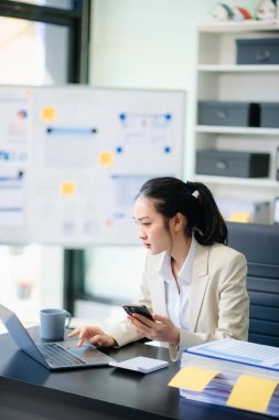 Telefonla konuşan gülümseyen Asyalı kadın. Genç, pozitif kadın muhasebeci. Akıllı telefon kullanıyor.