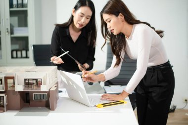 Tablet ve dizüstü bilgisayarda ev modelini ve dijital planları inceleyen mimarlar, modern mimari konsepti, gayrimenkul geliştirme, konut tasarımı ve profesyonel takım çalışması.