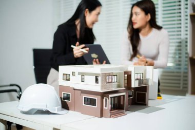 Tablet ve dizüstü bilgisayarda ev modelini ve dijital planları inceleyen mimarlar, modern mimari konsepti, gayrimenkul geliştirme, konut tasarımı ve profesyonel takım çalışması.