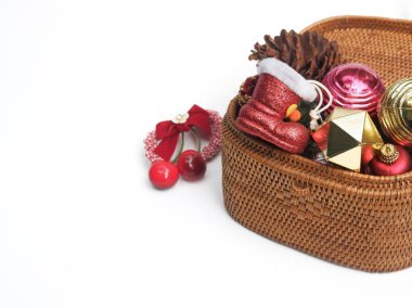 Renkli Noel süslemeleri ve aksesuarlarıyla dolu bir hasır sepet içinde minyatür kırmızı çizme, çam kozalağı ve beyaz arka planda bolca fotokopi alanı olan tatil mücevherleri de var..