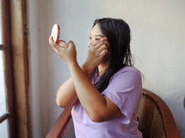 Pencere kenarındaki aynaya bakarken ruj süren bir kadın. Günlük güzellik rutini ve kozmetik konsepti.