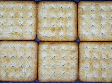 Yakın çekim, tam kare 6 kare tuzlu kraker bisküvisi 2x3 'lük bir ızgarada sıkıca dizilmiş. Üniforma deseni ve altın rengi çıtır çıtır olan dokuyu ön plana çıkarıyor ve güçlü bir yemek arkaplanı oluşturuyor..