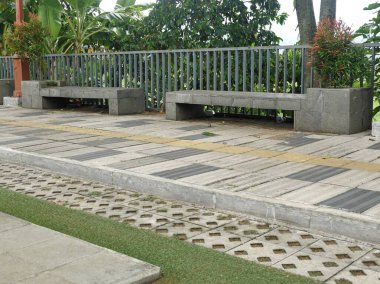 Çağdaş beton banklar ve metal korkuluklar yemyeşil yapraklı kentsel ya da şehir parkında bir kaldırım ve desenli kaldırım kenarında.