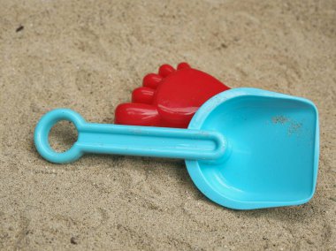Canlı mavi kürek ve kırmızı ayak izi kum kalıbı açık kumun üzerinde duruyor. Çocukların yaz tatili ve kumdan kale inşaatı için klasik aletler..
