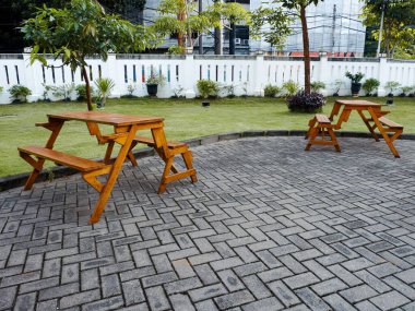 İki ahşap piknik masası ve taştan kaldırımlı ve yeşil çimenlikli, bakımlı bir açık hava bahçesinde yer alan banklar. Ağaçlar ve beyaz bir duvarla çevrili huzurlu bir oturma yeri..