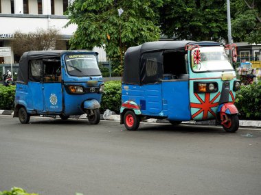 İki mavi tekerlekli bajaj triportör şehrin caddesine park etmiş. Geleneksel bir Jakarta taşıma aracında renkli özel çıkartmalar.