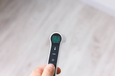 Beyaz arka planda kızılötesi dijital termometreyi tutan bir elin yakın çekimi. Akıllı sağlık, hijyen ve modern tıp teknolojisi kavramı.