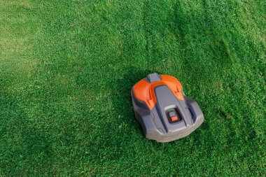 Mükemmel kesilmiş yeşil çimenlikte modern robot çim biçme makinesi otomasyonu, akıllı ev teknolojisini ve zahmetsiz bahçe bakımını sembolize ediyor..