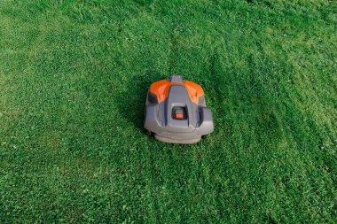 Mükemmel kesilmiş yeşil çimenlikte modern robot çim biçme makinesi otomasyonu, akıllı ev teknolojisini ve zahmetsiz bahçe bakımını sembolize ediyor..