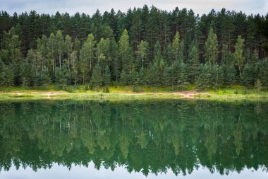 Durgun sulara yansıyan sık yeşil ormanlı sakin göl manzarası huzurlu bir doğal manzara yaratıyor..