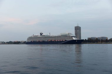 Modern çoklu güverte yolcu gemisi yumuşak bir akşam gökyüzünün altındaki yüksek bir binanın yakınındaki limana yanaştı..