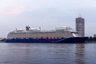 Modern çoklu güverte yolcu gemisi yumuşak bir akşam gökyüzünün altındaki yüksek bir binanın yakınındaki limana yanaştı..