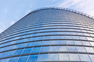 Mavi gökyüzünü ve bulutları yansıtan cam pencereli çağdaş ofis binasının düşük açılı görüntüsü.