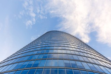 Mavi gökyüzünü ve bulutları yansıtan cam pencereli çağdaş ofis binasının düşük açılı görüntüsü.
