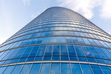 Mavi gökyüzünü ve bulutları yansıtan cam pencereli çağdaş ofis binasının düşük açılı görüntüsü.