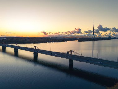 Günbatımında geniş bir nehri geçen uzun ve modern bir pilon köprüsünün alacakaranlık görüntüsü..