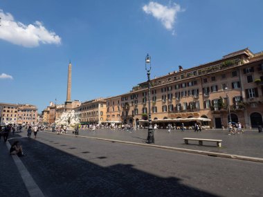 Roma 'daki Piazza Navona Meydanı' nın geniş bir manzarası var. Dört Nehir Çeşmesi dikilitaş kaldırım, açık hava restoranları, güneşli bir yaz gününde Roma binaları ve turistler.