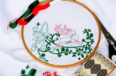White tablecloth in a round frame being embroidered with Christmas scene.