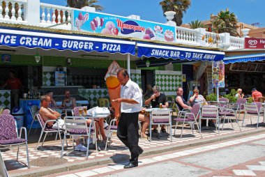 Tourists relaxing in pavement cafes on promenade, Benalmadena. clipart