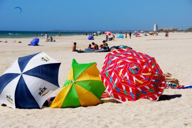 Ön planda renkli plaj şemsiyeleri ile beyaz kumlu plajda dinlenen turistler, El Palmar.