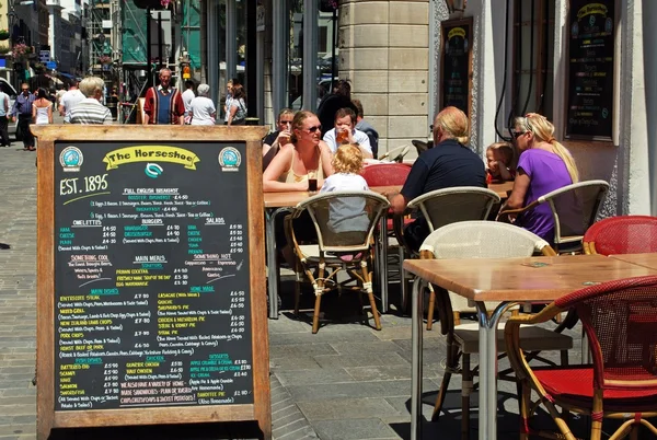 Turistas relaxando no pub Horseshoe ao longo da Main Street com uma placa de menu na rua, Gibraltar . — Fotografia de Stock