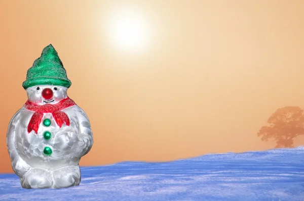 Glass Christmas snowman ornament against a snowy sunrise. — Stock Photo, Image