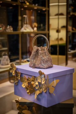 Milan, İtalya - 2026, 13 Ocak: Işıldayan Jimmy Choo FW25 el çantası şık bir butik ortamında altın renkli çiçek aksanlı dekoratif bir mor kutunun üzerinde sergilendi