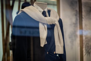 Milan, İtalya - 2026, 3 Şubat: Brunello Cuccinelli FW25 vitrininde rafine edilmiş bir donanma takımı ve bej örgü eşarbı sergilenmektedir.