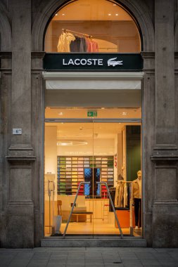 Milan, İtalya - 2026, 3 Şubat: Zarif taş cepheli Lacoste FW25 butiği, modern cam girişi ve şık bir şehir ortamında aydınlatılmış moda gösterileri