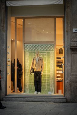Milan, İtalya - 2026, 3 Şubat: Lacoste FW25 vitrin vitrininde şık, modern bir vitrinde yeşil tasarımcı arka planı ve modaya uygun şehir modasına sahip şık bir manken yer alıyor